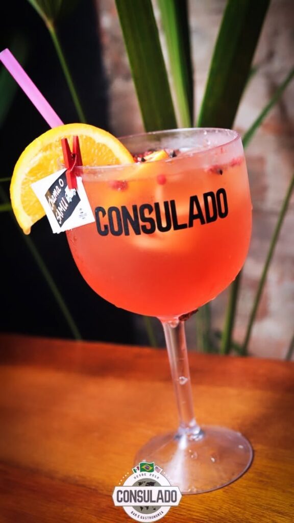 consulado-bar-campo-largo- drink avermelhado em cima da mesa com um pedaço de limão na borda e uma etiqueta com uma mensagem escrita